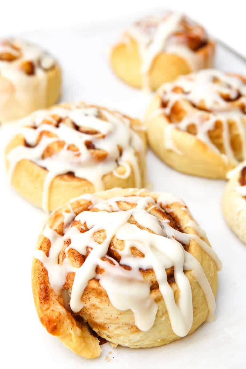 Six vegan cinnamon rolls on a cookie sheet drizzled with icing.