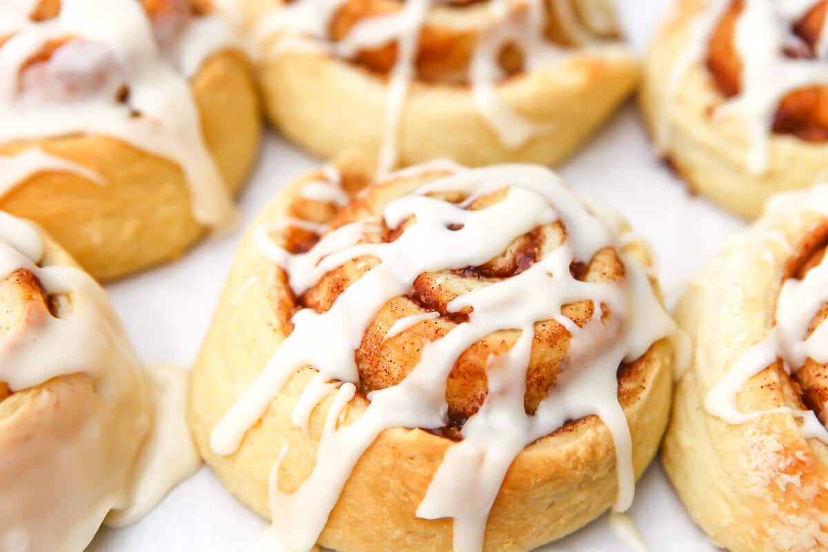 Six vegan cinnamon rolls with vegan cream cheese icing drizzled on top of them.