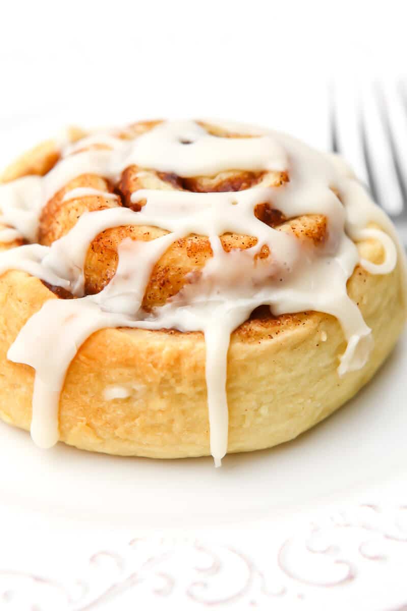 A vegan cinnamon roll on a white plate with a fork on the side.