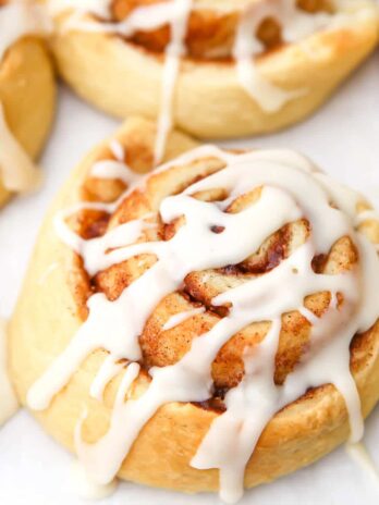A close up of a vegan cinnamon bun with icing drizzled on top.