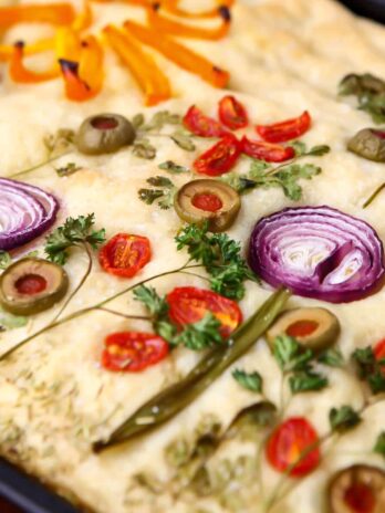 A close up of vegan focaccia bread decorated with veggies to look like flowers on top.