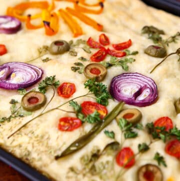 A close up of vegan focaccia bread decorated with veggies to look like flowers on top.