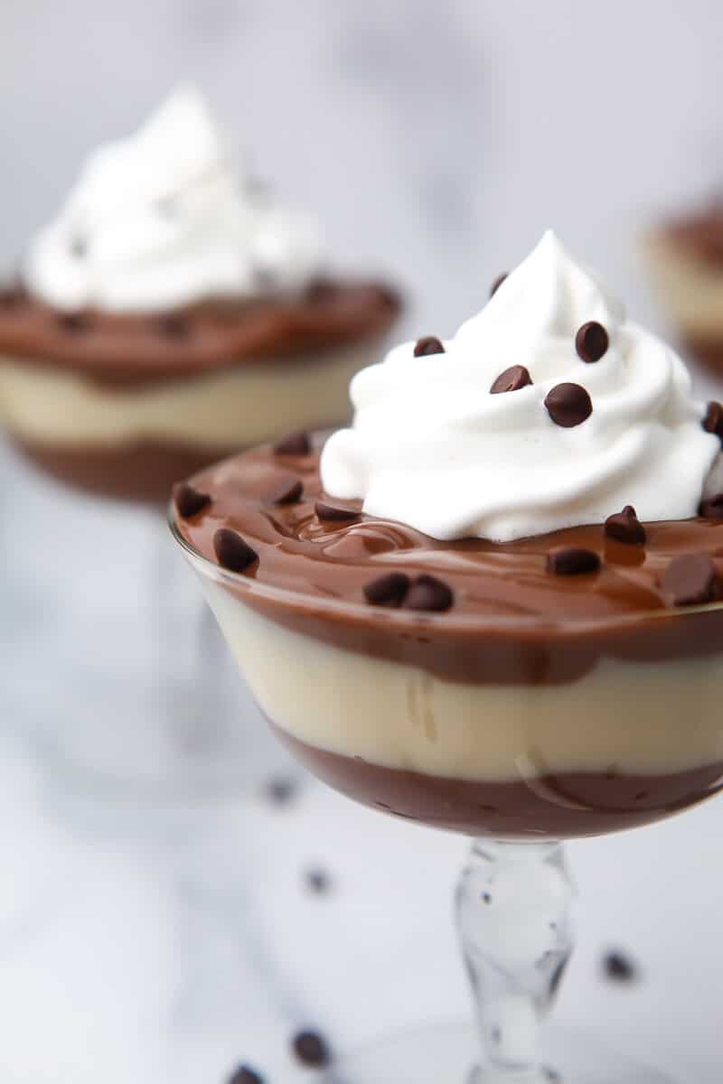 Vegan chocolate pudding and vanilla pudding layered in a glass with vegan whipped cream on top.