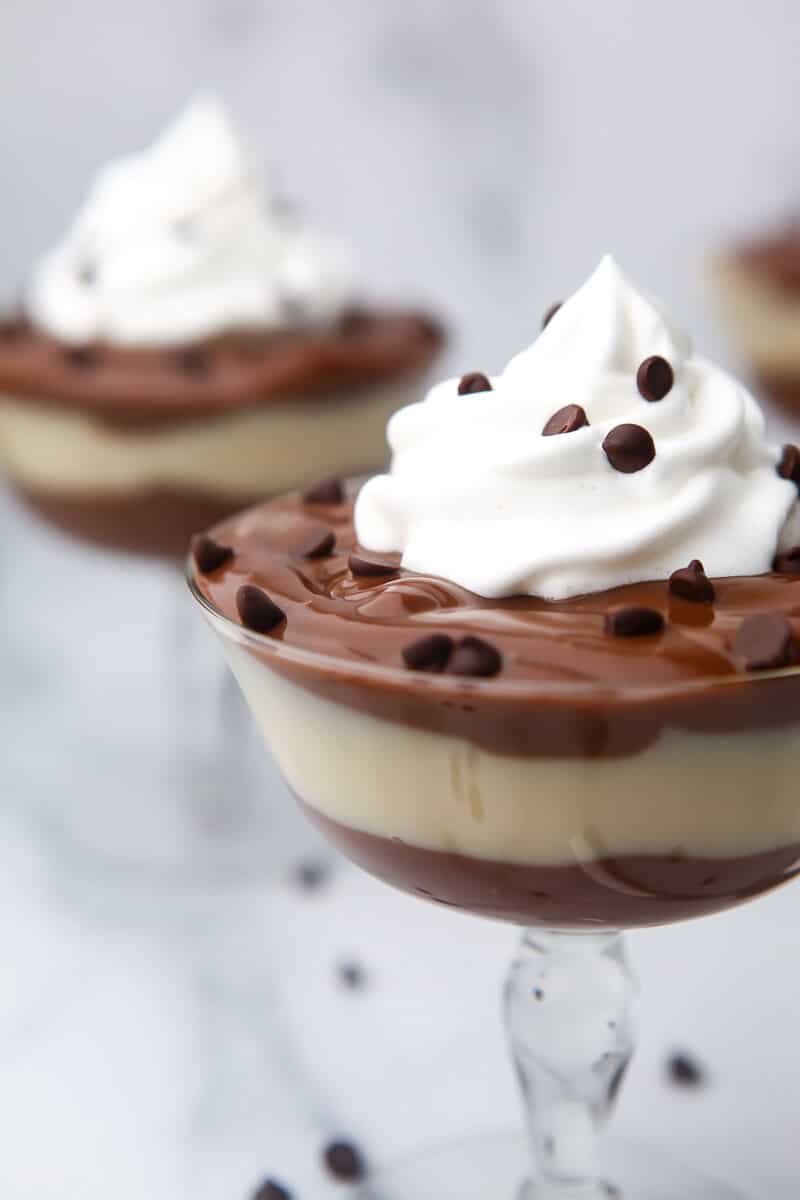 Vegansk chokladpudding och vaniljpudding i lager i ett glas med vegansk vispgrädde på toppen.