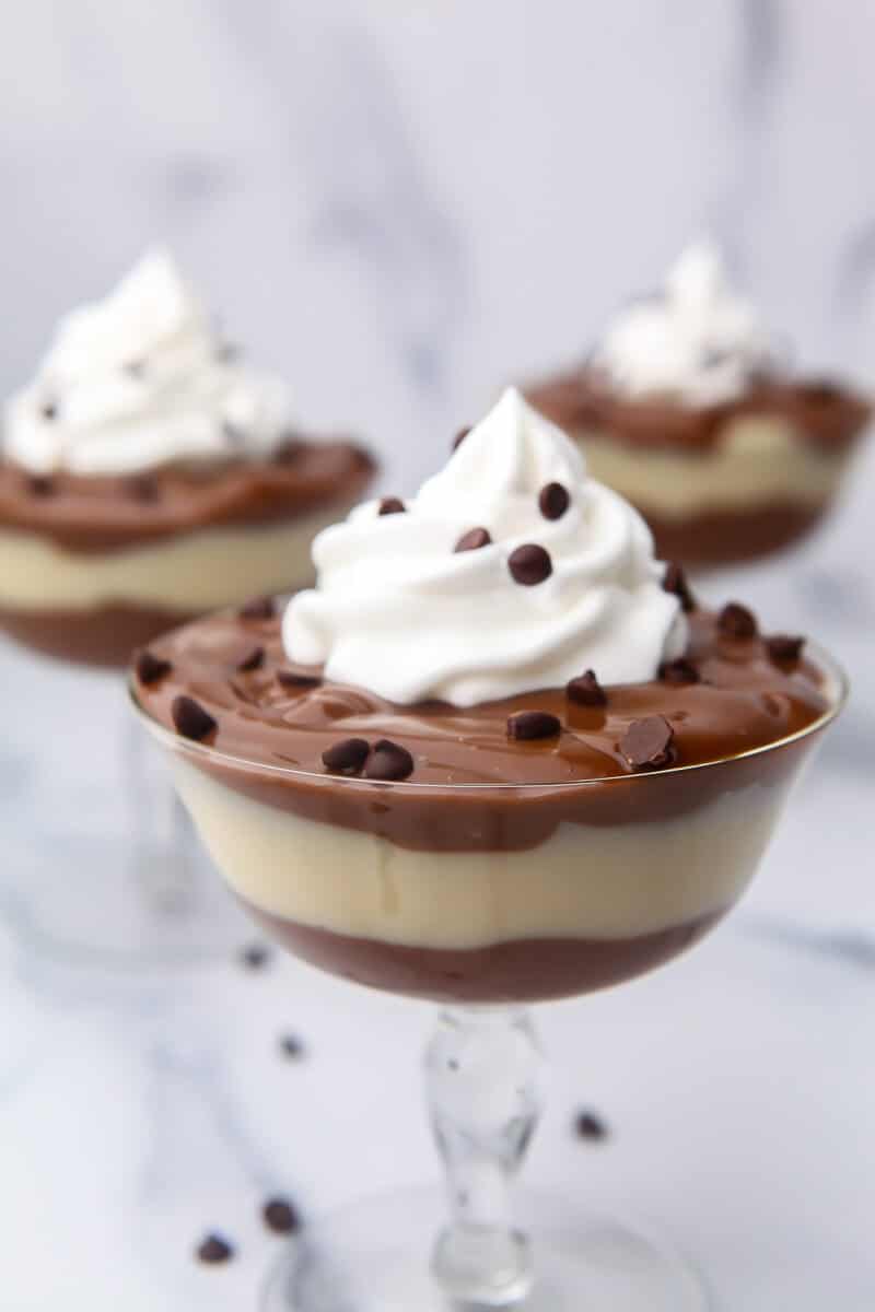 Three clear glasses filled with layers of vegan pudding topped with whipped cream.