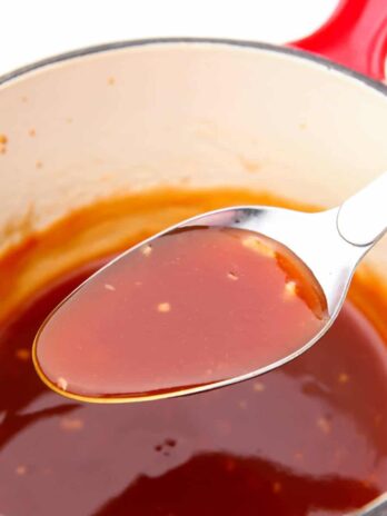 A spoonful of sweet and sour sauce being held over a sauce pot after cooking.