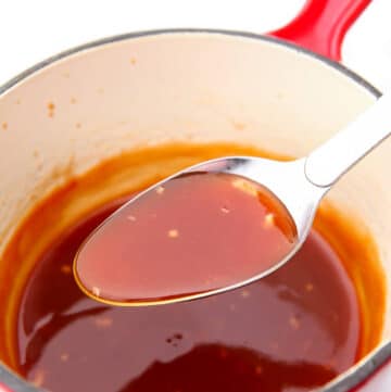 A spoonful of sweet and sour sauce being held over a sauce pot after cooking.