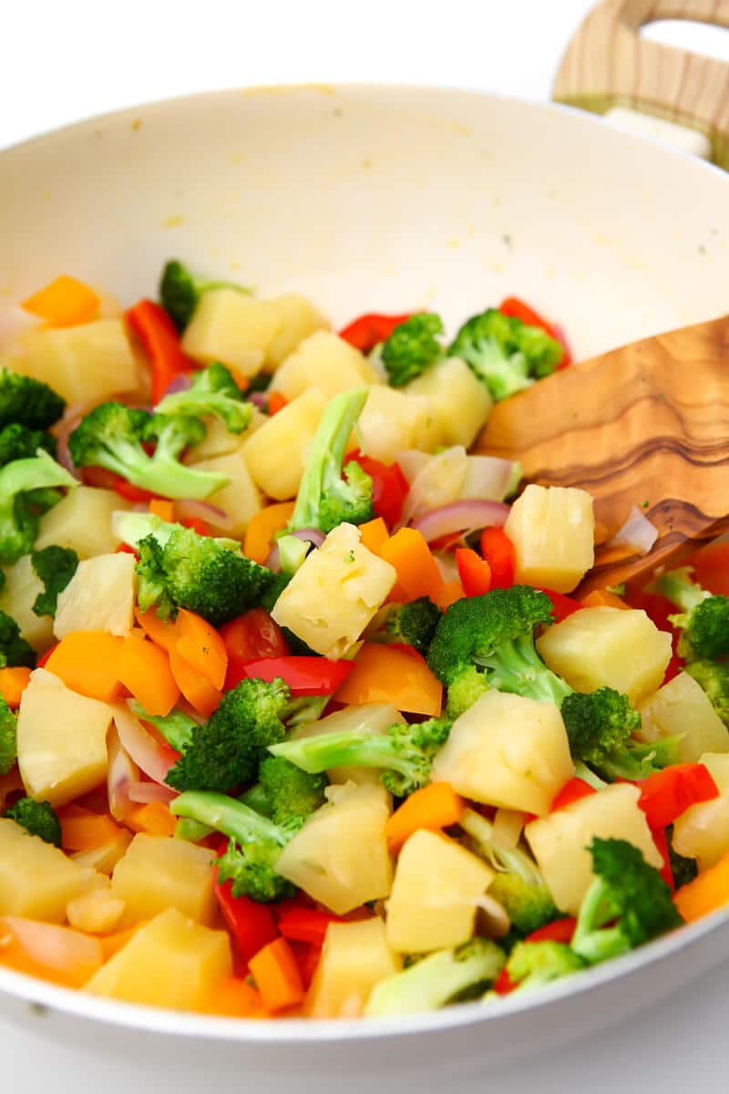 Mixed veggies and cubed pineapple in a wok being cooked.