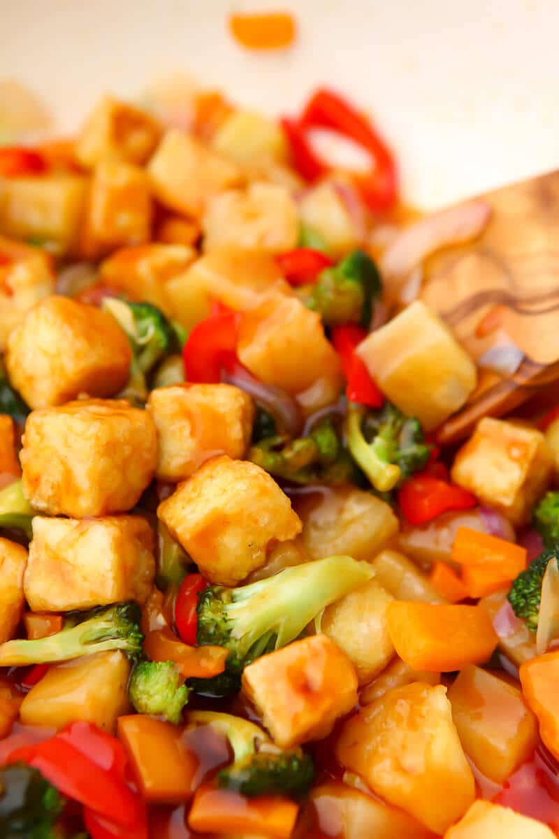 A close up of sweet and sour tofu with veggies and pineapple in a white wok.