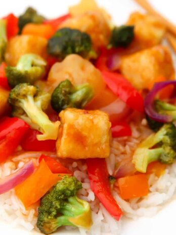 Sweet and sour tofu with veggies over rice on a white plate.