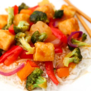 Sweet and sour tofu with veggies over rice on a white plate.