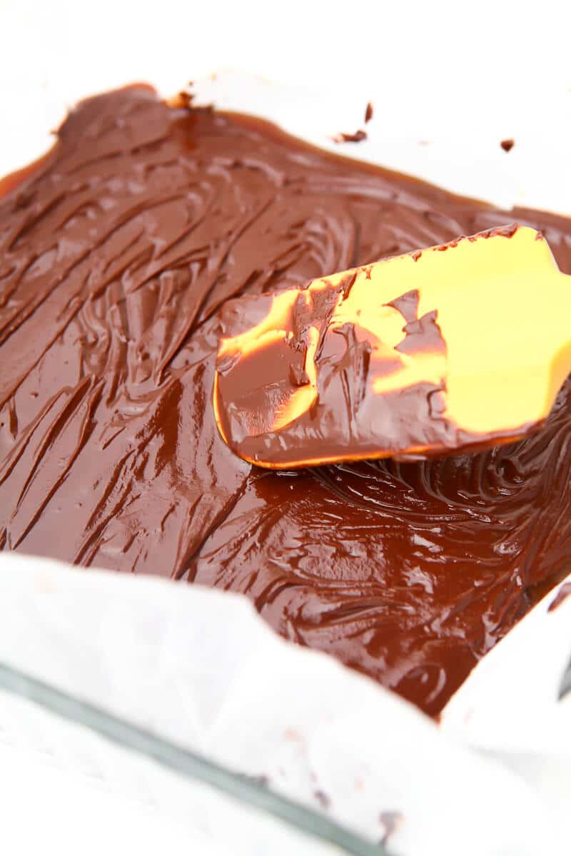 Vegan chocolate being spread over layers of shortbread and caramel to make vegan millionaire shortbread bars.