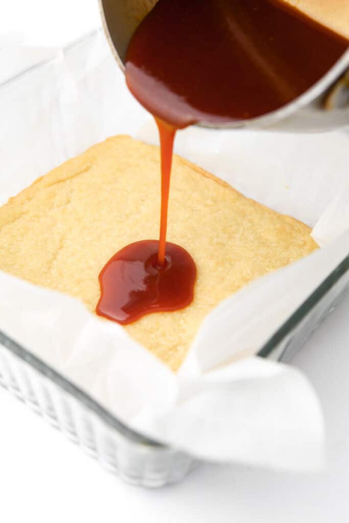Vegan caramel being poured onto cooked shortbread to make millionaire bars.