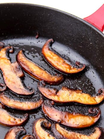 Sliced portabella mushrooms cooking in a skillet.