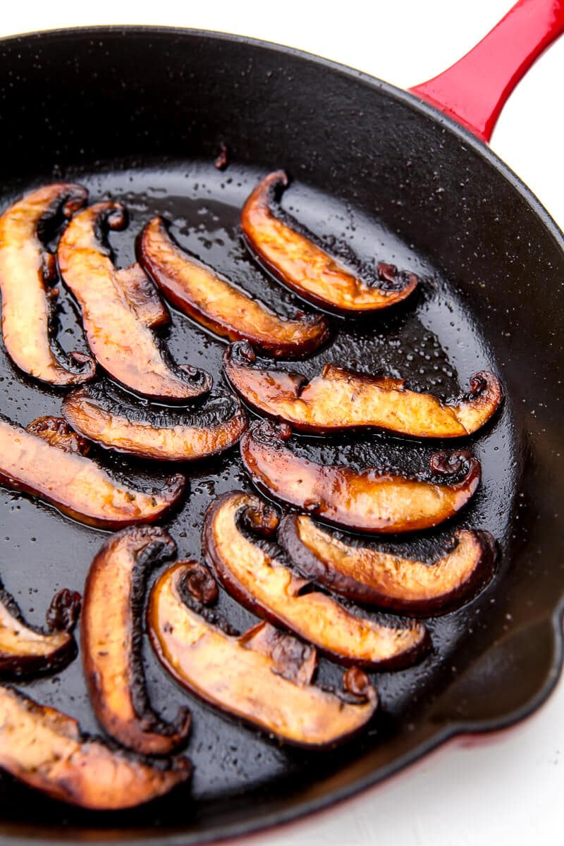 Mushroom bacon cooking in an iron skillet with a red handle.
