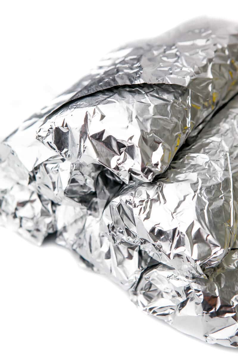 A stack of breakfast burritos wrapped in foil ready to freeze.