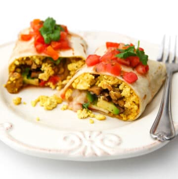 A vegan breakfast burrito cut in half with salsa and cilantro on top.
