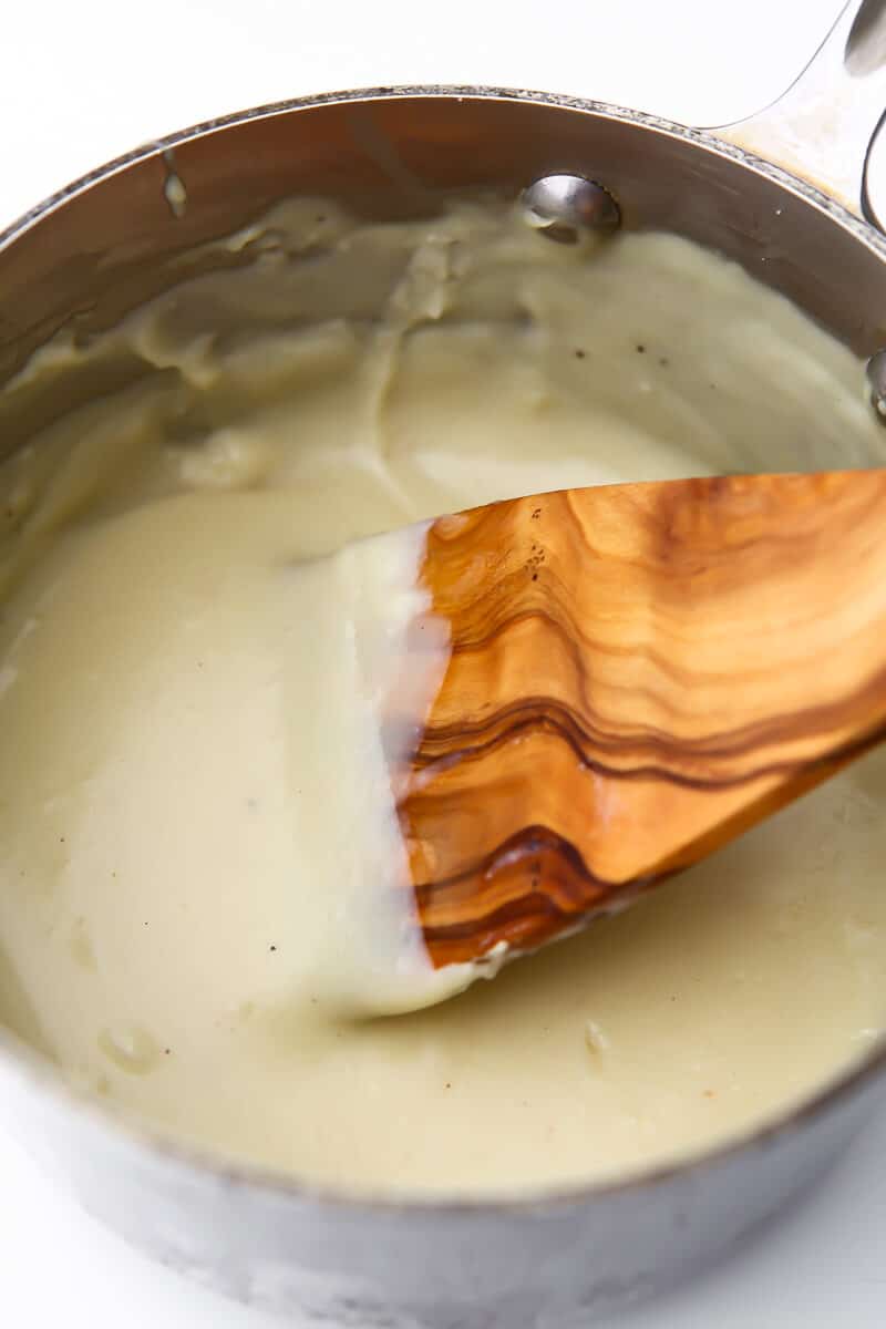 A saucepan with vegan Bechamel sauce in it being stirred with a wooden spoon