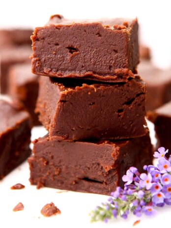 A stack of three pieces of vegan chocolate fudge with a purple flower and more pieces of fudge around it.