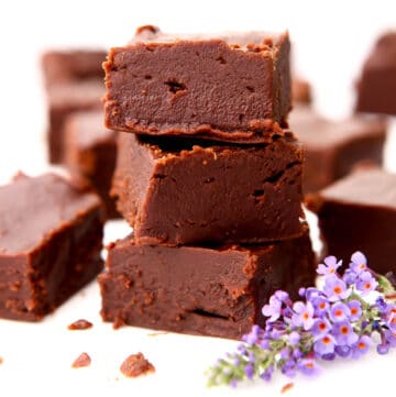 A stack of three pieces of vegan chocolate fudge with a purple flower and more pieces of fudge around it.