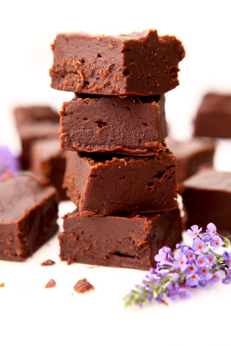 Four pieces of vegan fudge stacked on top of each other with a purple flower next to it.