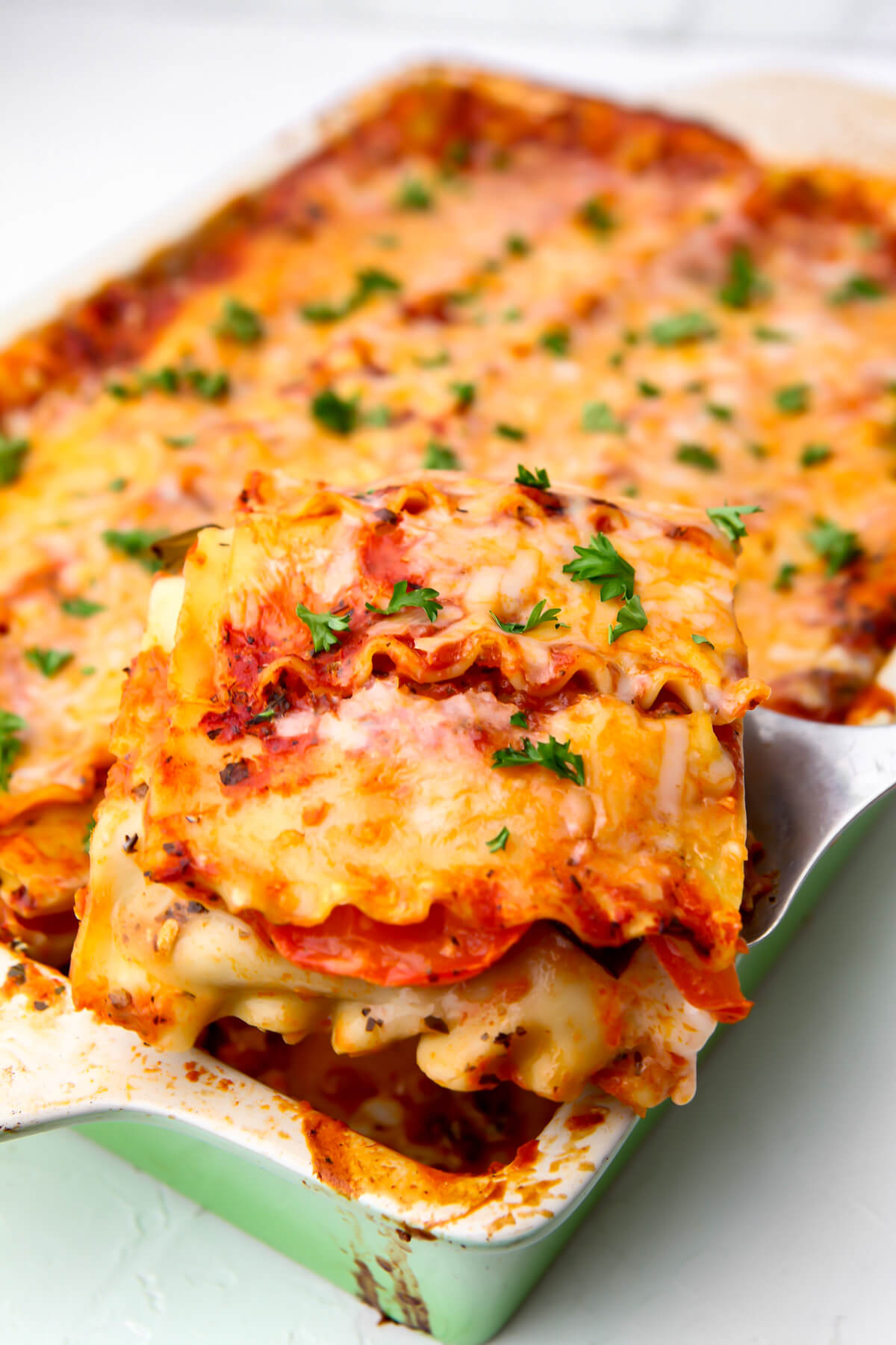 A slice of vegan lasagna being taken out of the baking dish with a spatula.