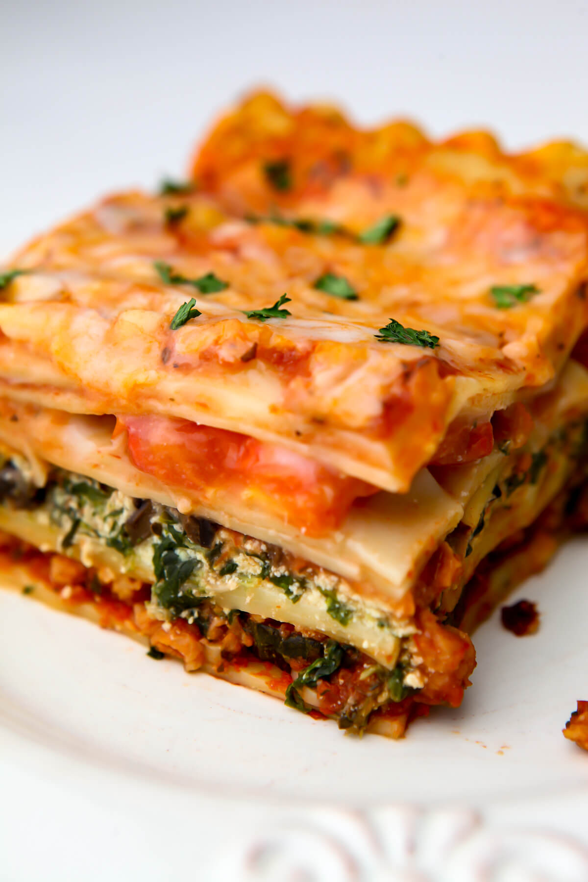 A piece of vegetarian lasagna with layers of tofu ricotta, spinach, tomatoes and vegan cheese.