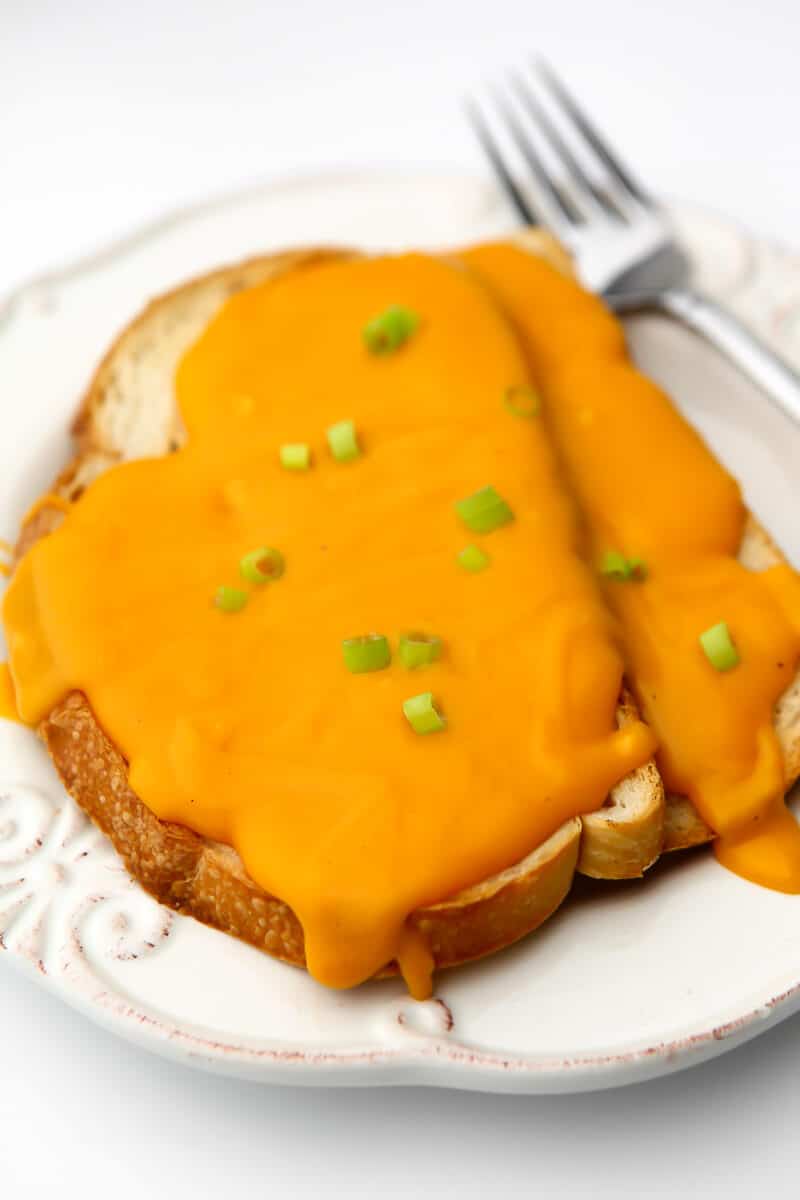 A vegan Welch Rarebit sauce served over 2 pieces of toast with a fork on the side.