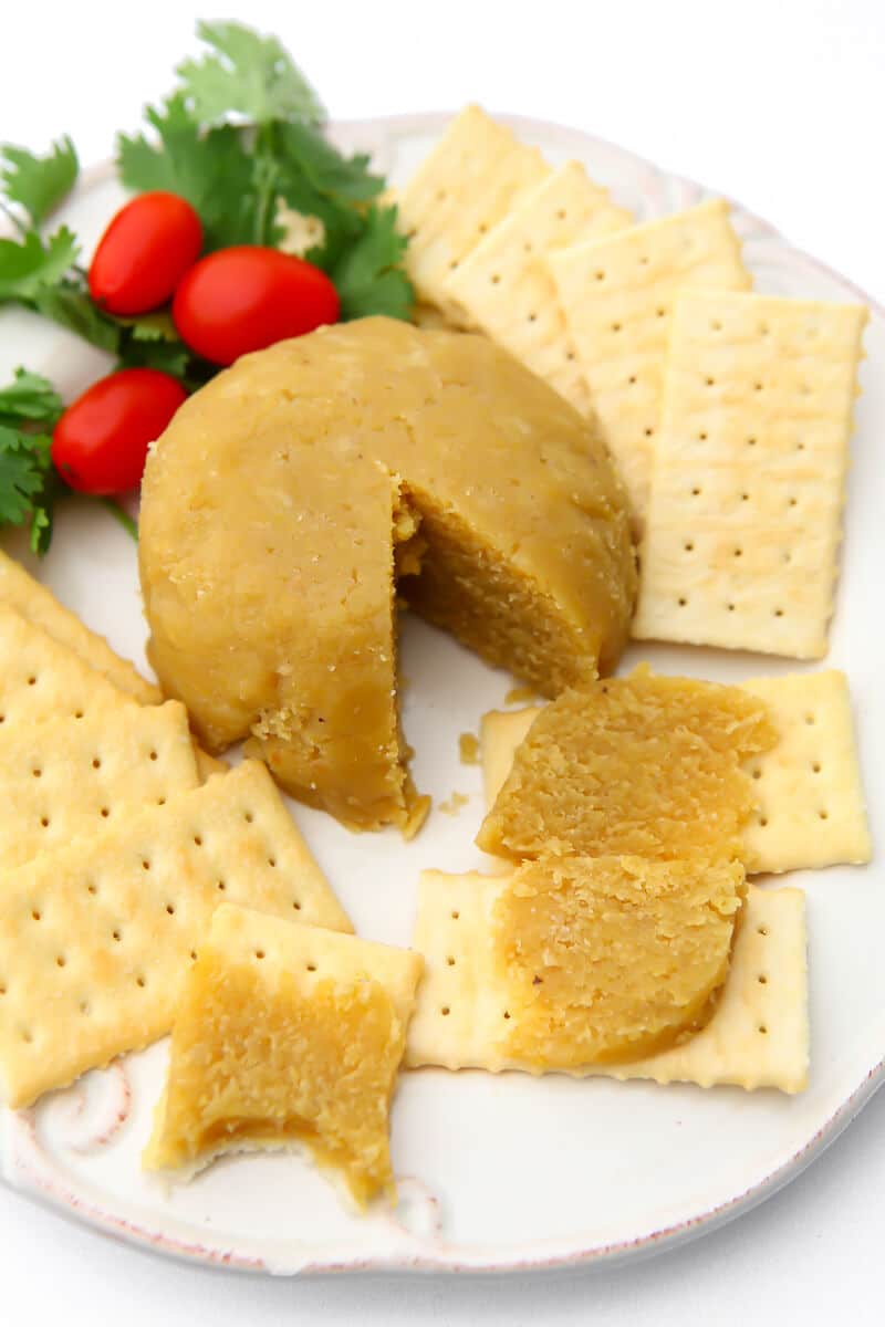 A round of almond cheese on a white plate with crackers around it.