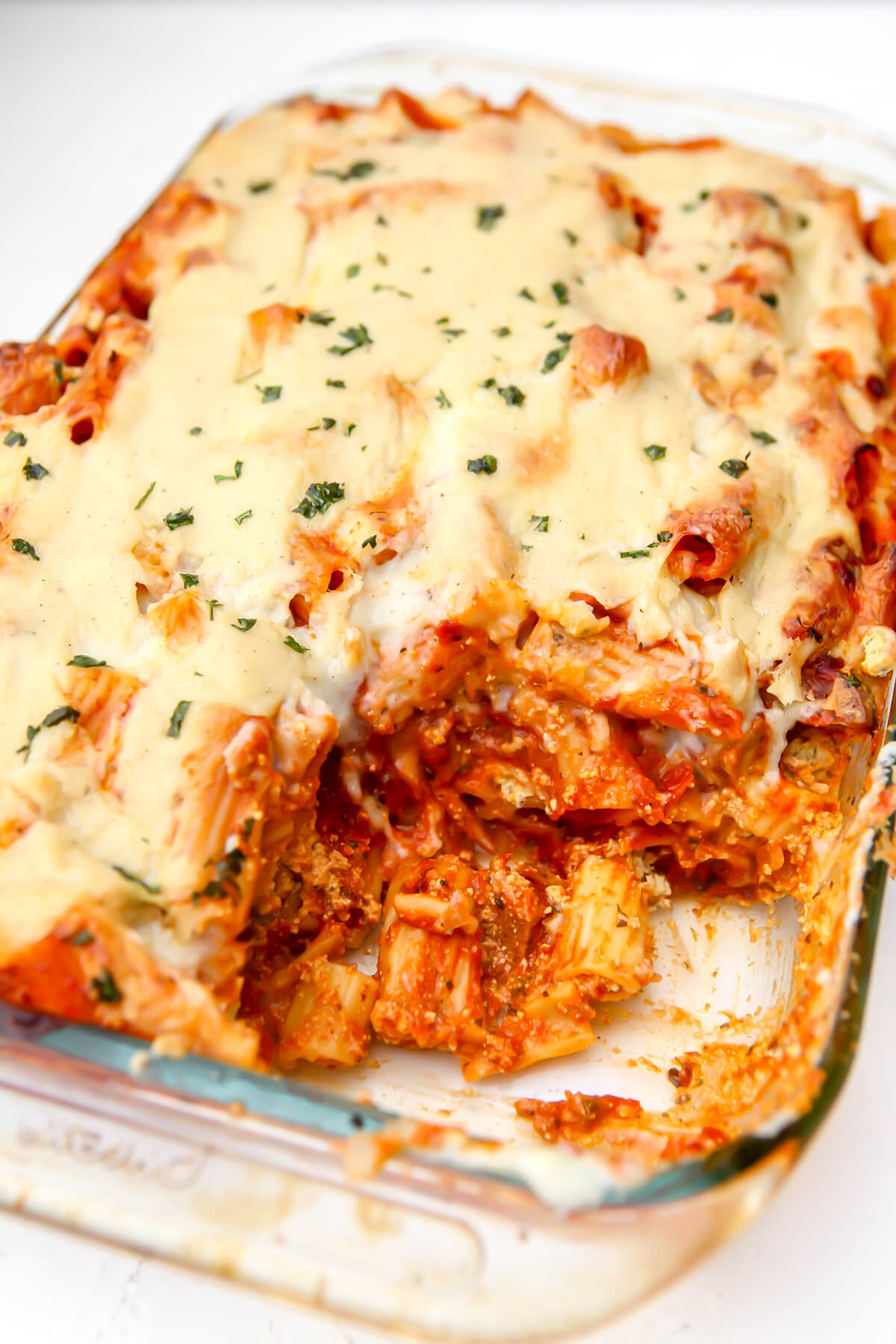 A casserole dish filled with vegan baked ziti with tofu ricotta with a scoop taken out.