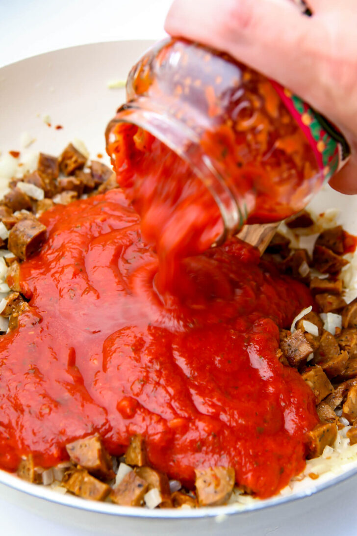 Adding pasta tomato sauce to the onions, and sausage.