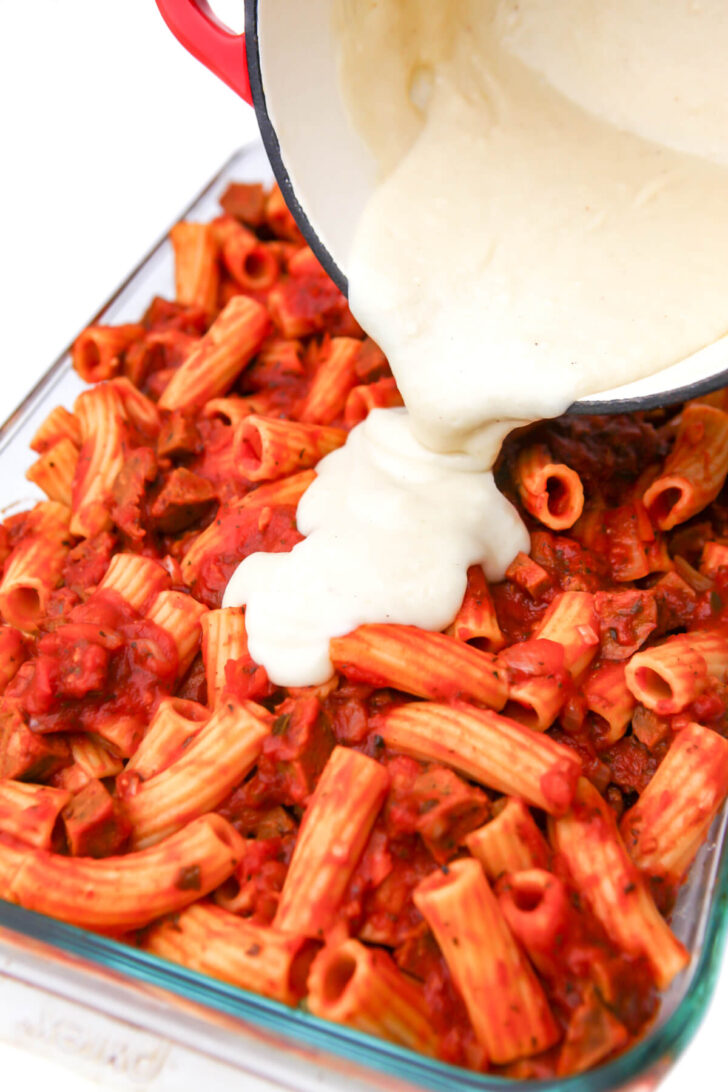 Vegan béchamel sauce being poured over the ziti pasta. 