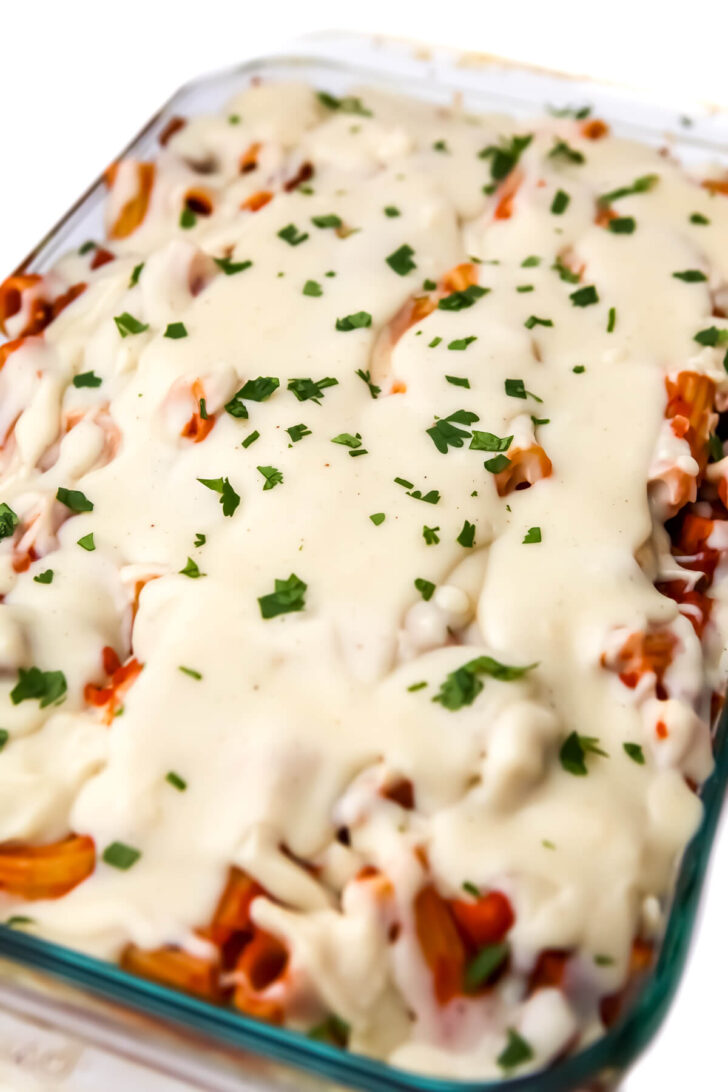 A vegan baked ziti topped with béchamel sauce and sprinkled with parsley.