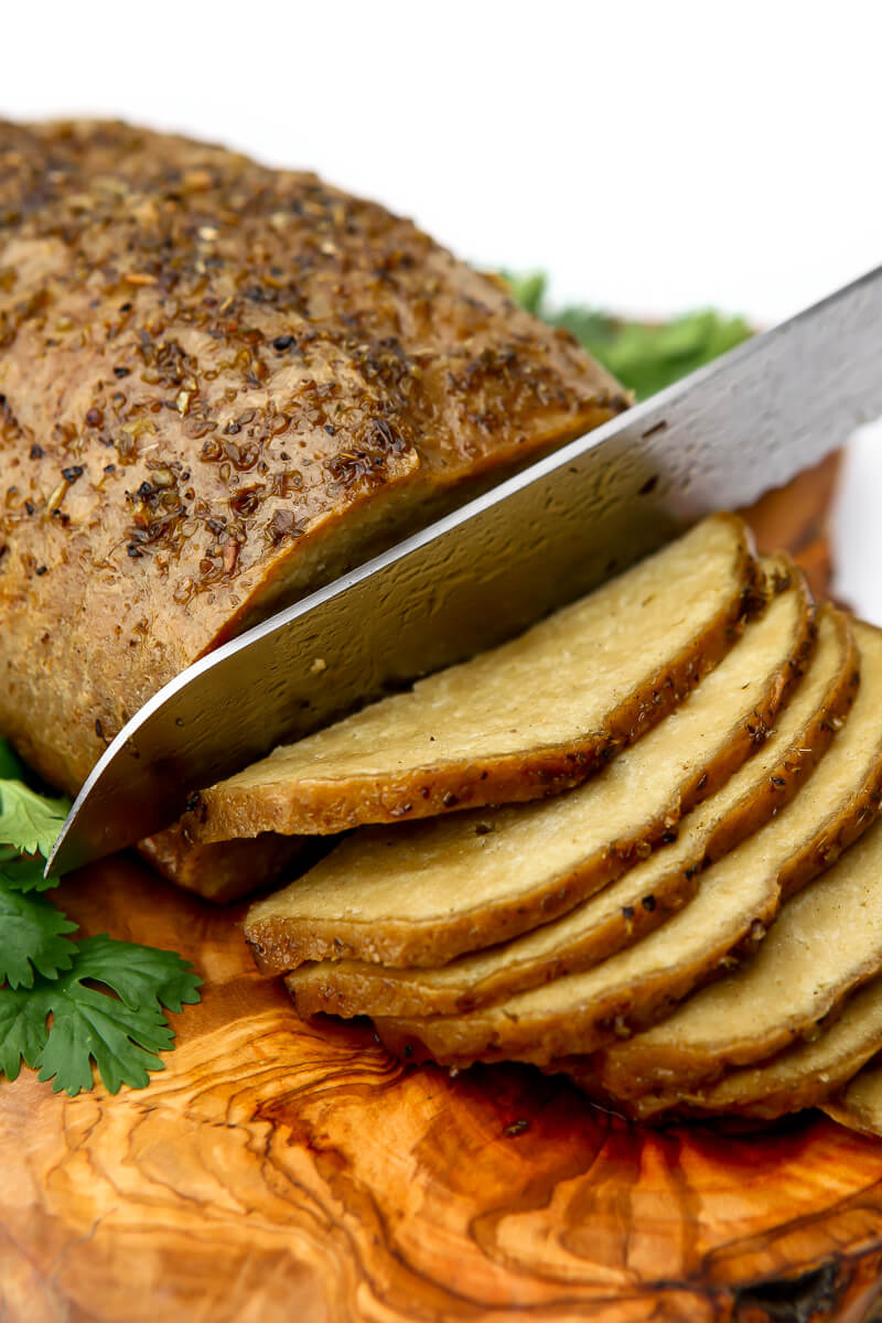 A vegan tofurkey on a cutting board being cut into slices with parsley on the sides.