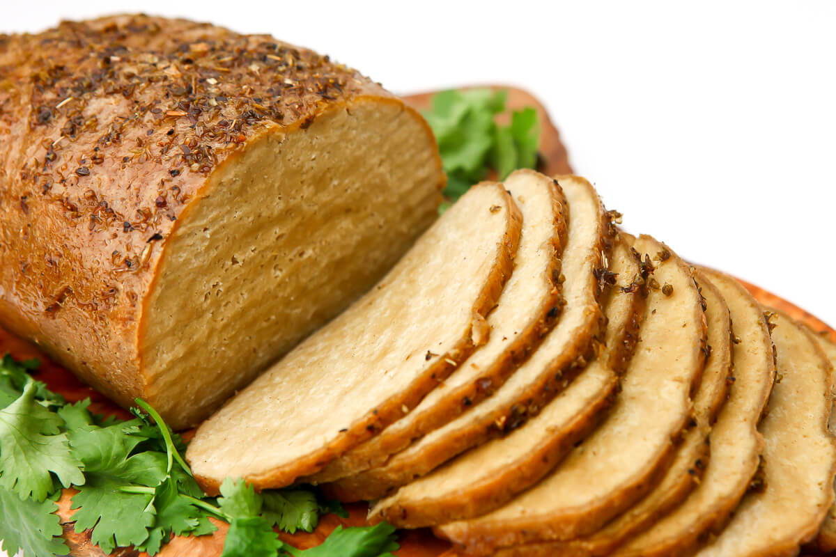 A vegan turkey loaf on a cutting board cut into slices.