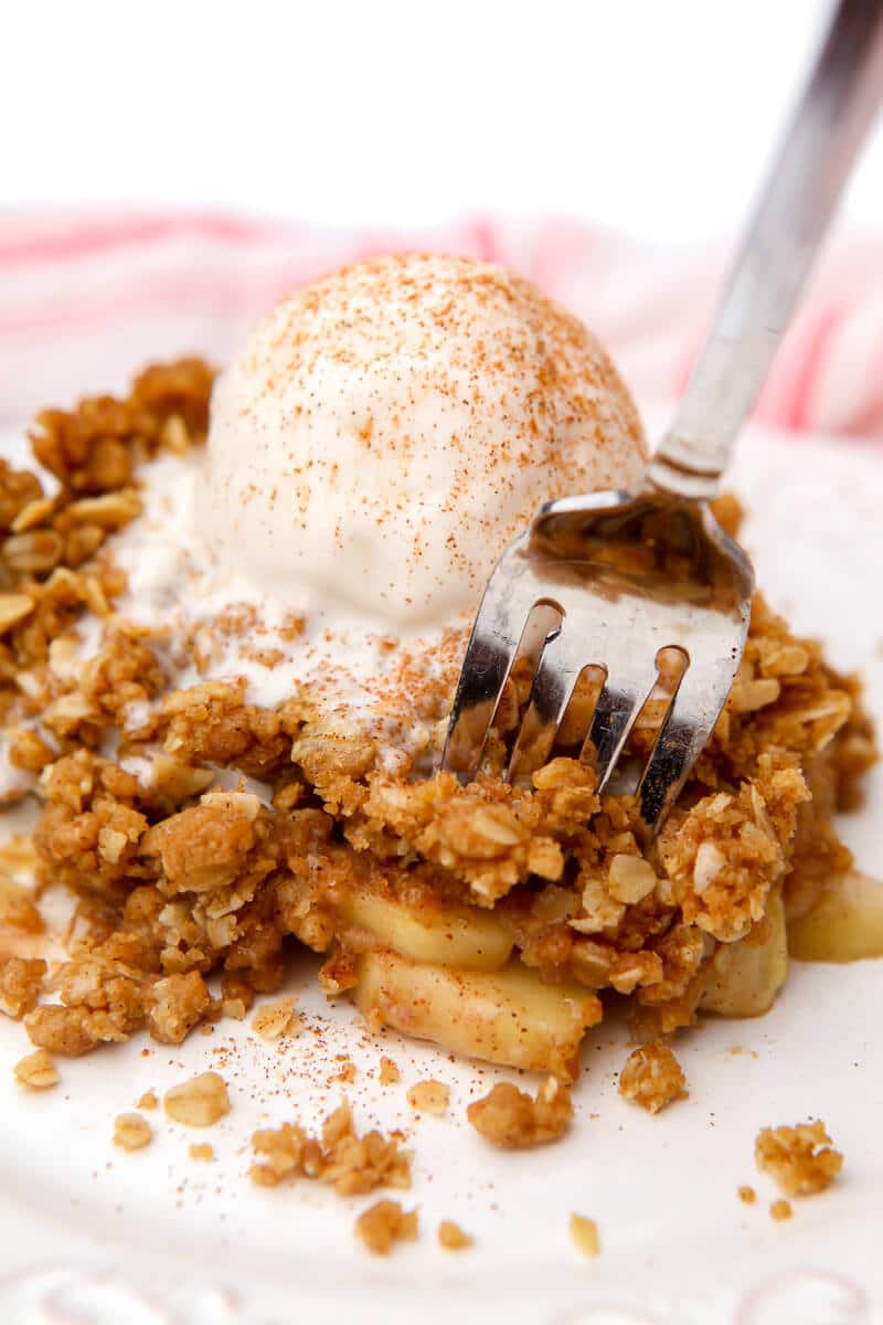 A helping of vegan apple crisp with icecream on top with a fork in it.