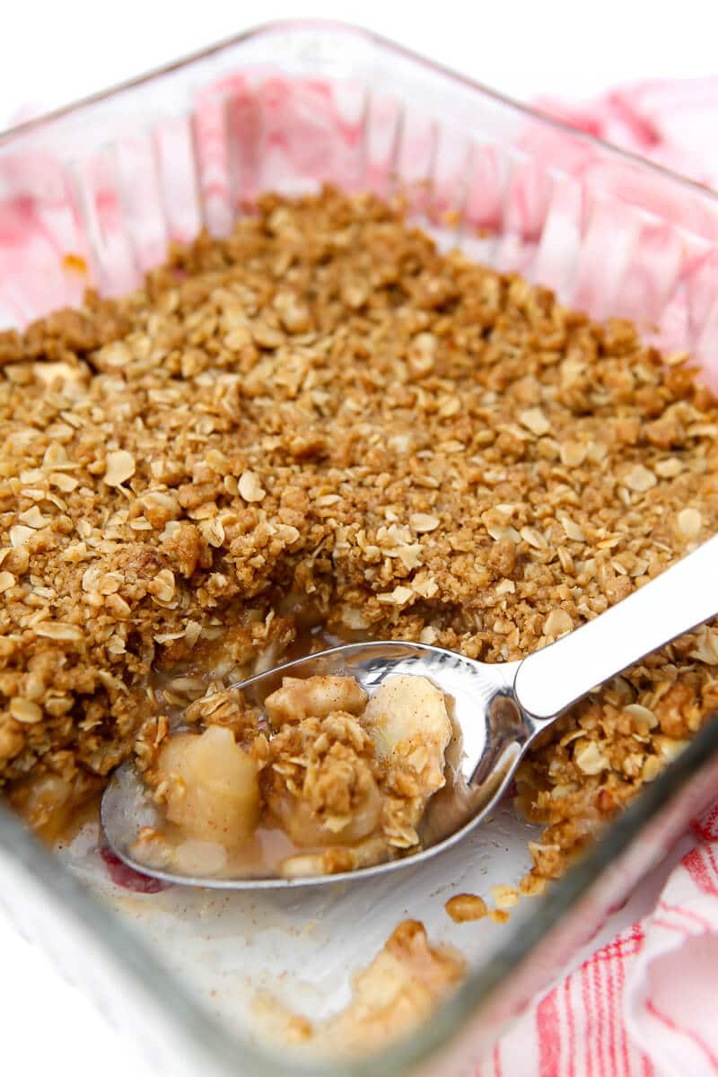 A baking dish filled with vegan apple crisp with a thick layer of crumble topping and a piece taken out of it.