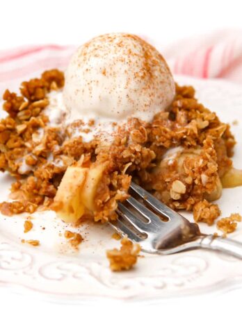 A large slice of vegan apple crisp with a scoop of vanilla icecream on top with some loaded on a fork.