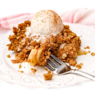 A large slice of vegan apple crisp with a scoop of vanilla icecream on top with some loaded on a fork.