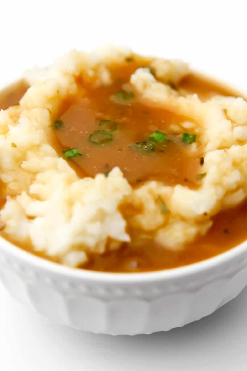 A white bowl filled with mashed potatoes with brown gravy poured over top.