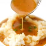 A close up of vegan brown gravy being poured over mashed potatoes.