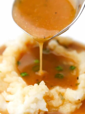 A close up of vegan brown gravy being poured over mashed potatoes.