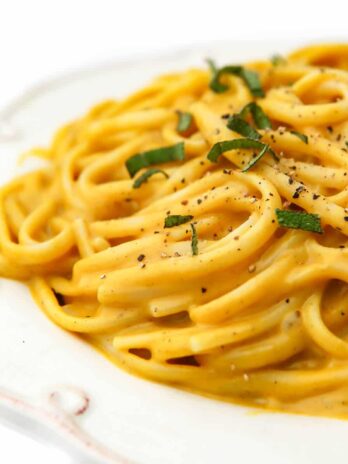 A white plate filled with vegan pumpkin pasta sprinkled with fresh sage.