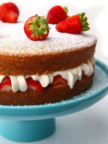 A vegan Victorian sponge cake with whipped cream and strawberries in the middle on a blue cake dish.