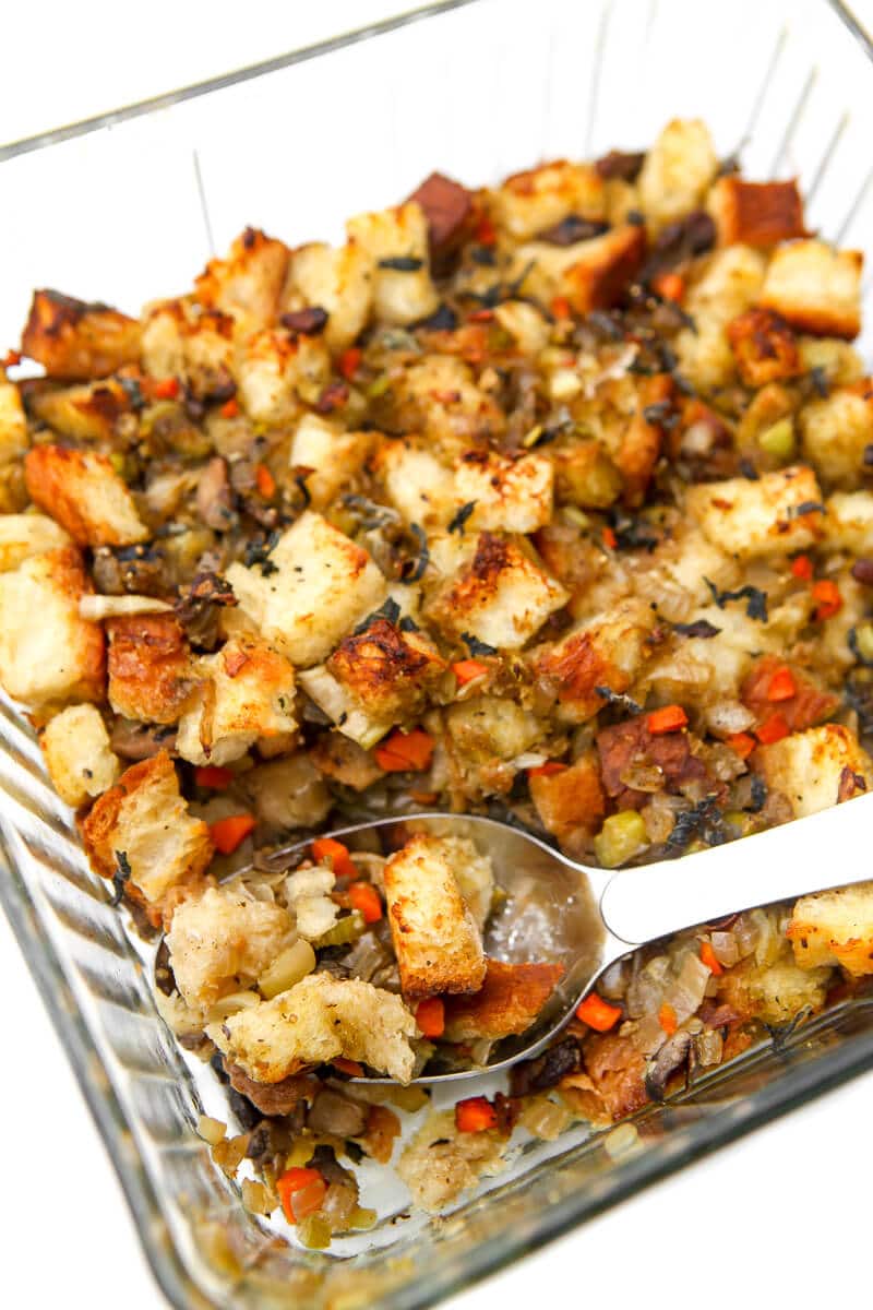 A square glass baking dish filled with vegan stuffing with a large spoon in it.