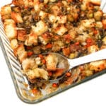 Baked vegan stuffing in a casserole dish with a large spoon taking some out.