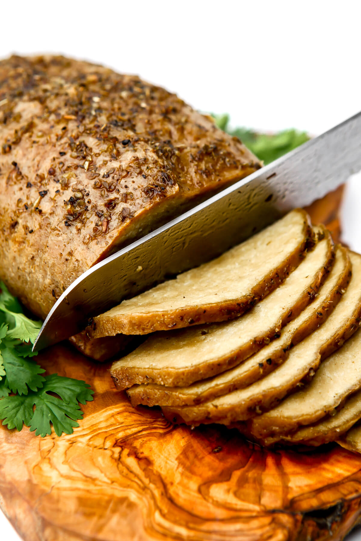 A vegan tofurkey on a cutting board being cut into slices with parsley on the sides.