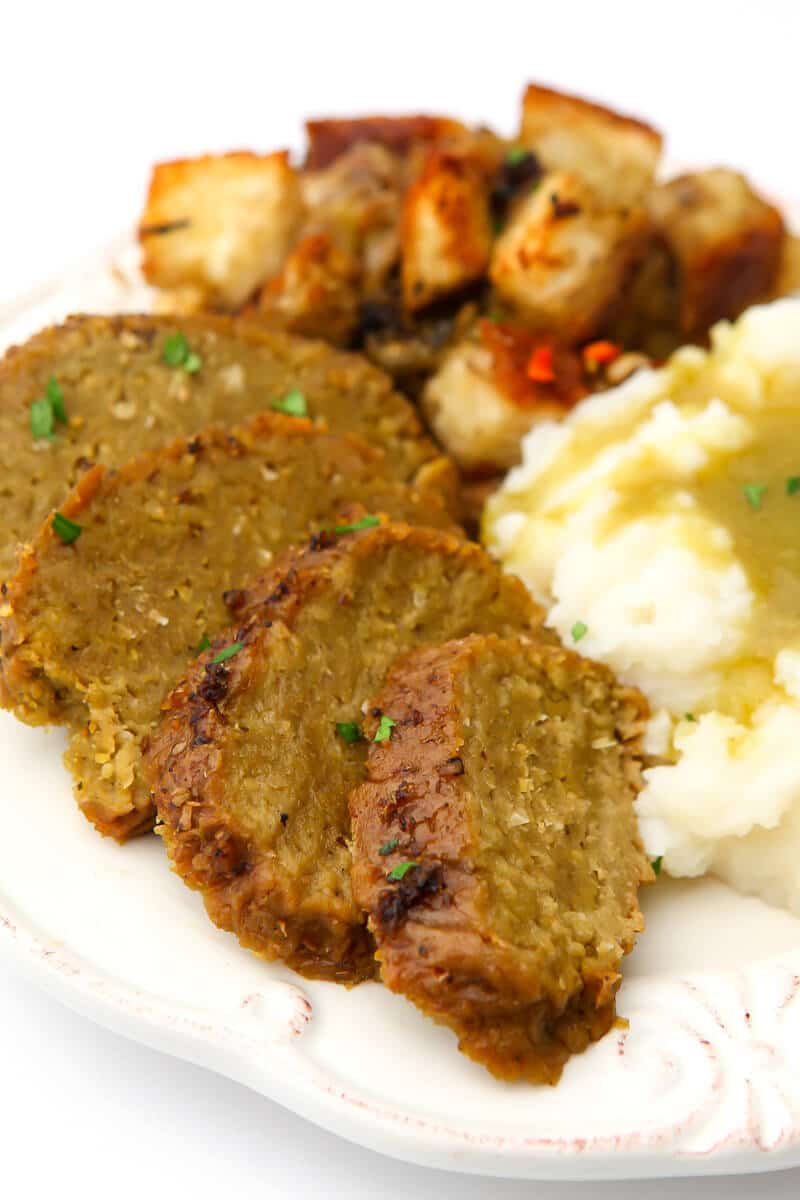 Sliced turkey seitan on a plate with stuffing, mashed potatoes and gravy. 