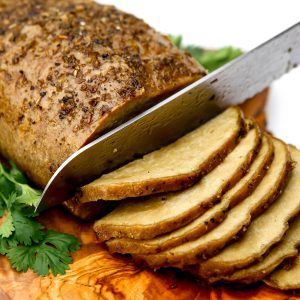 A vegan turkey made from seitan on a cutting board being sliced with a knife