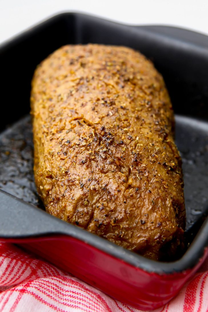 Vegan turkey basting in spices in a red baking dish.